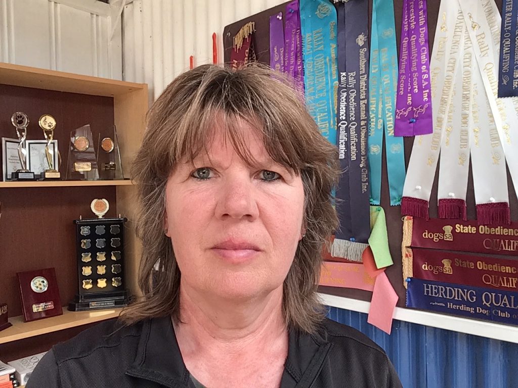 Woman looks into the camera with multiple trophies and prize ribbons in the background